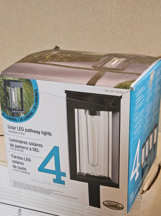 A 4-pack of vintage-style solar LED pathway lights in their original retail packaging, showing the front and side panels of the box.
