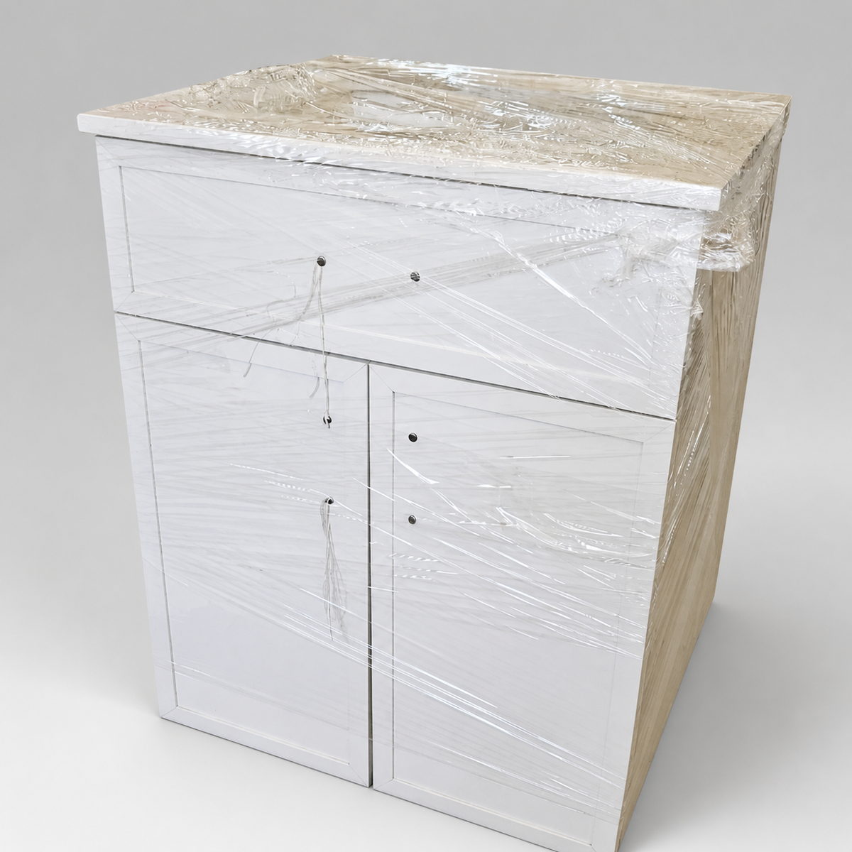 White freestanding storage cabinet with upper drawer and two lower doors, protective wrap intact